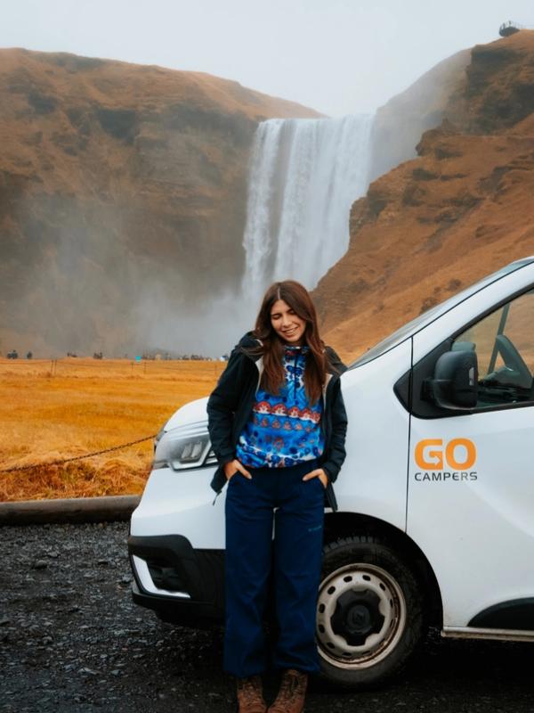 a woman is standing next to a white van in front of a waterfall .