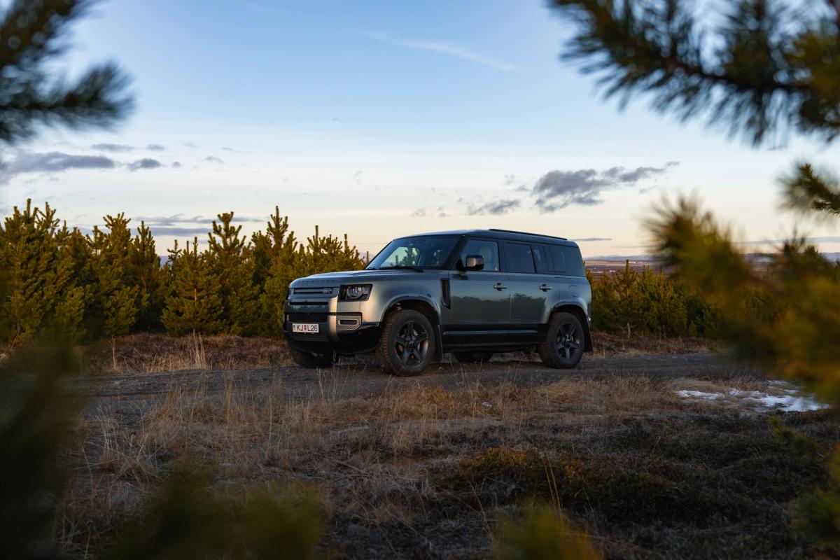Land Rover Defender de alquiler aparcado entre pinos al atardecer en Islandia, disponible para alquilar en Go Car Rental