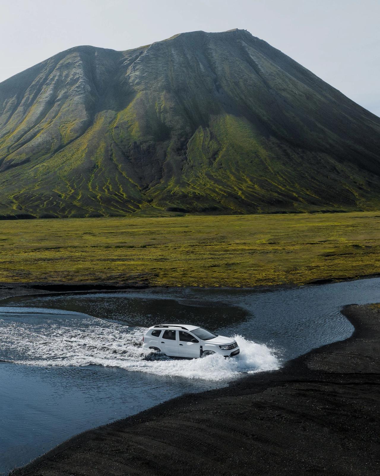 Dacia Duster SUV crossing a river in an F-road in Iceland surrounded by mountain