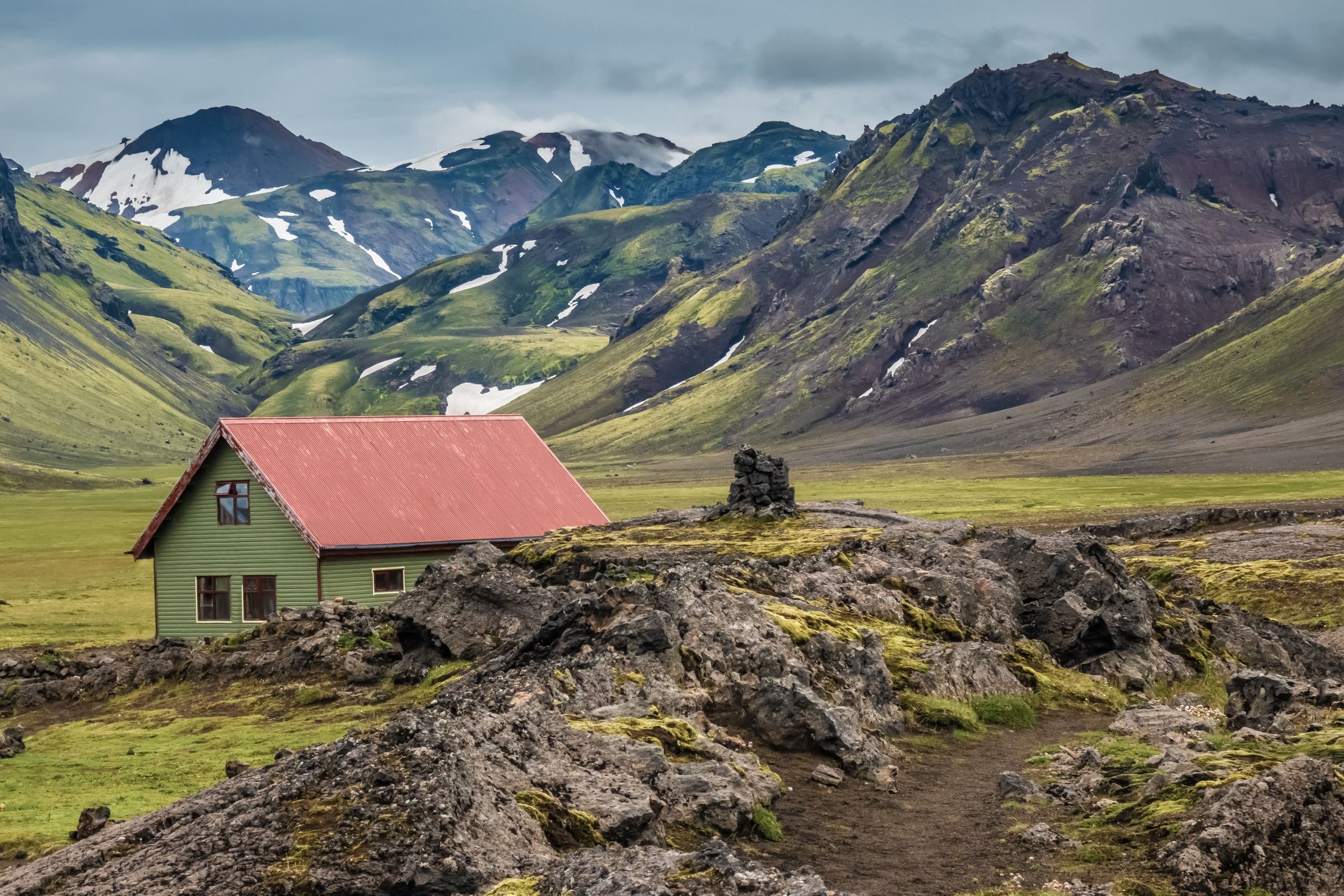 A green house with a red roof in a rocky, green mountain valley.