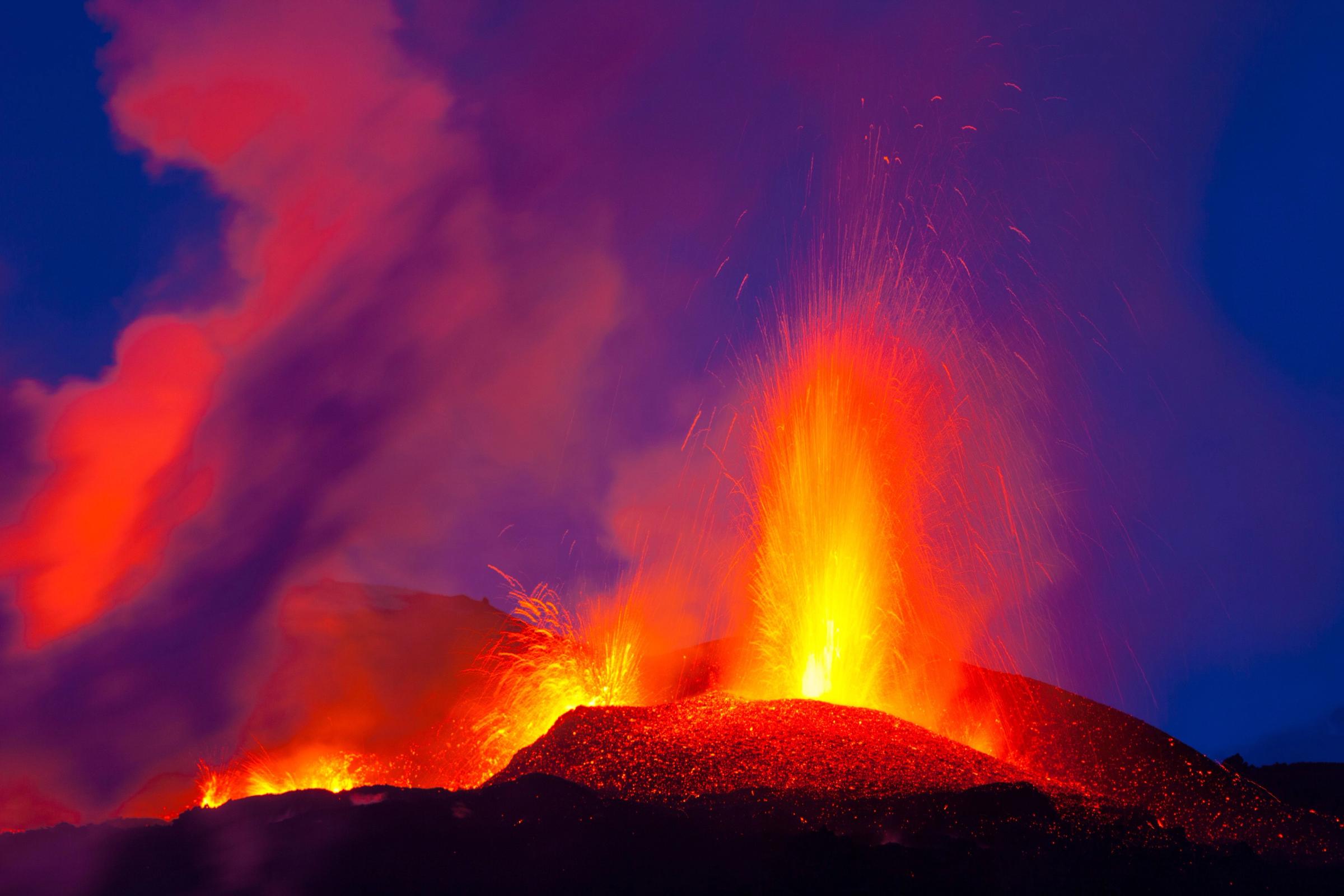 a volcano is erupting at night with a lot of lava coming out of it .