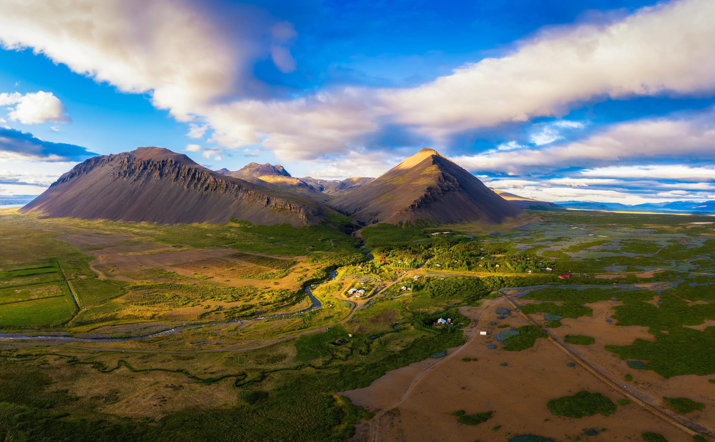 An aerial view of a green valley with a winding river between two large mountains under a dramatic cloudy sky.