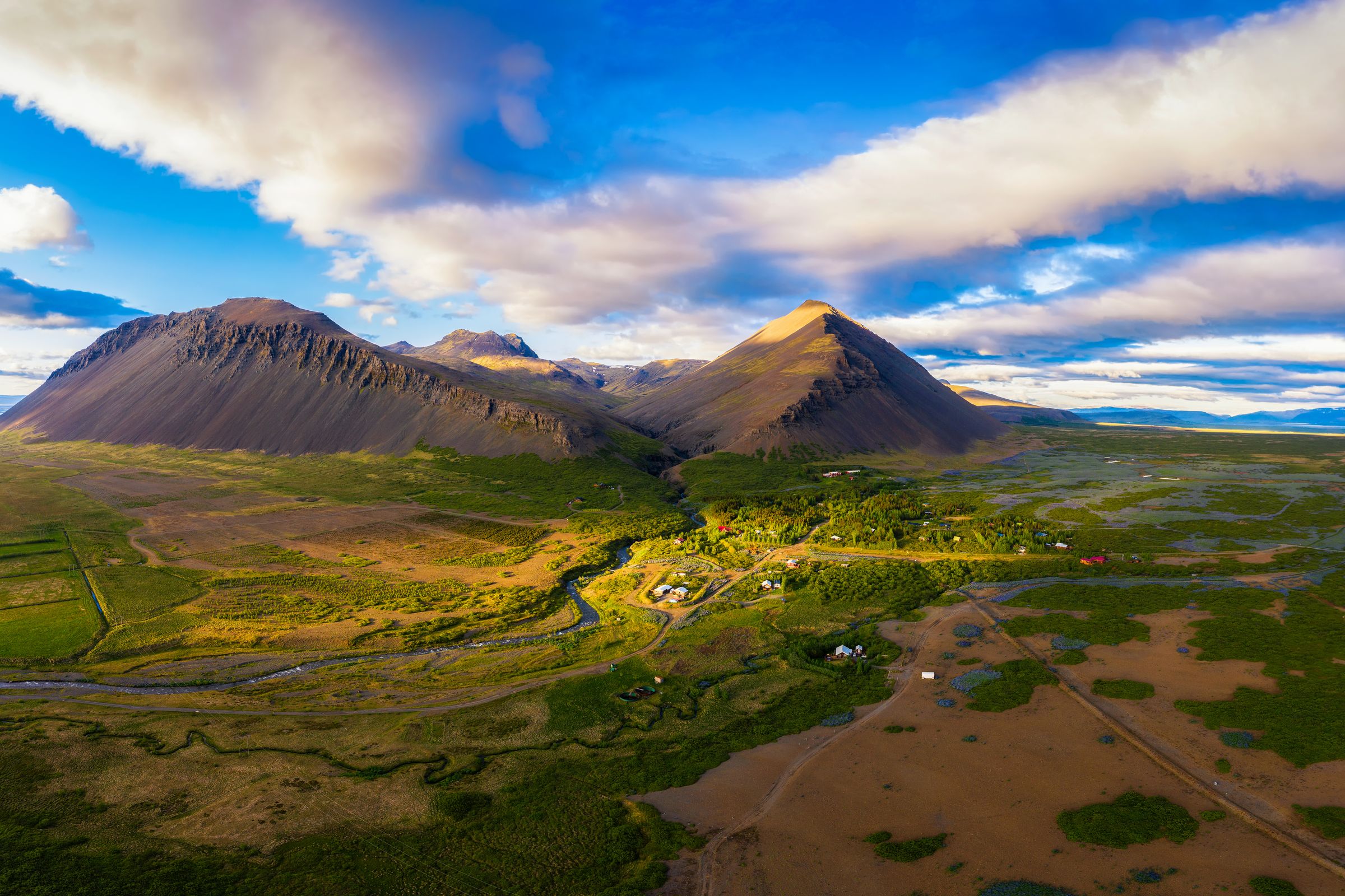 An aerial view of a green valley with a winding river between two large mountains under a dramatic cloudy sky.