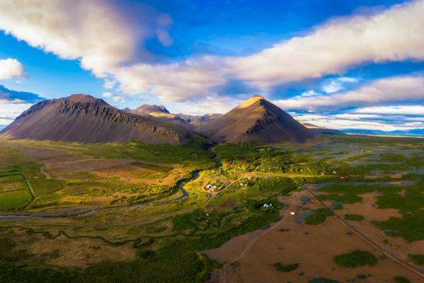 An aerial view of a green valley with a winding river between two large mountains under a dramatic cloudy sky.