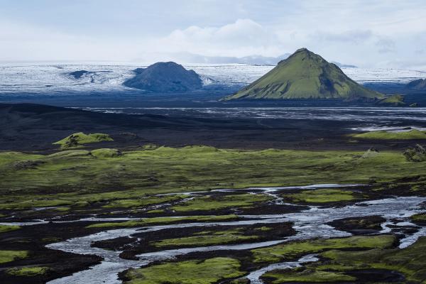 a river running through a grassy field with mountains in the background .