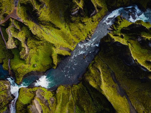 Aerial view of a vibrant green canyon with a winding river, waterfalls, and a viewing platform.
