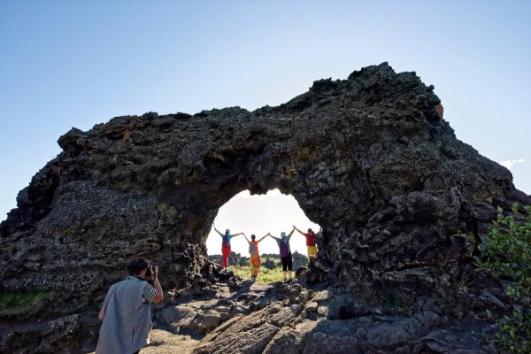 A person photographs four people holding hands, silhouetted under a dark natural arch.