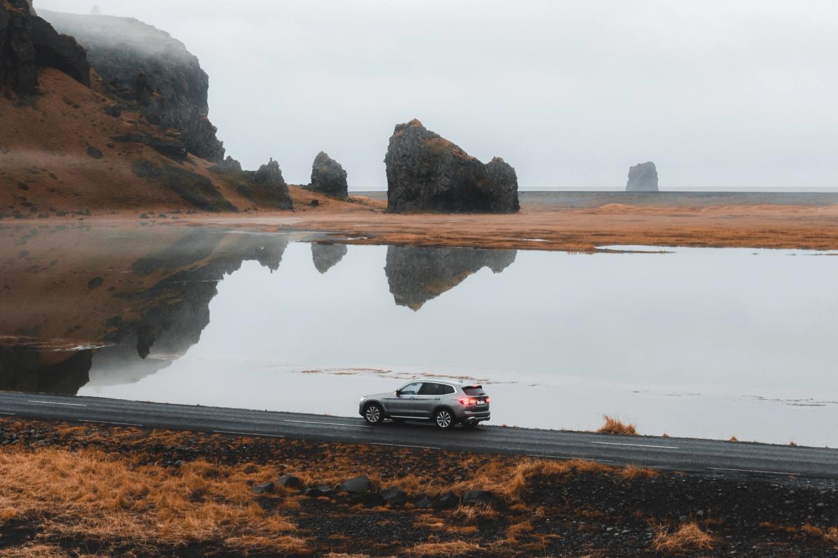 BMW X3 roulant sur une route côtière, avec des stacks marins se reflétant dans une eau calme