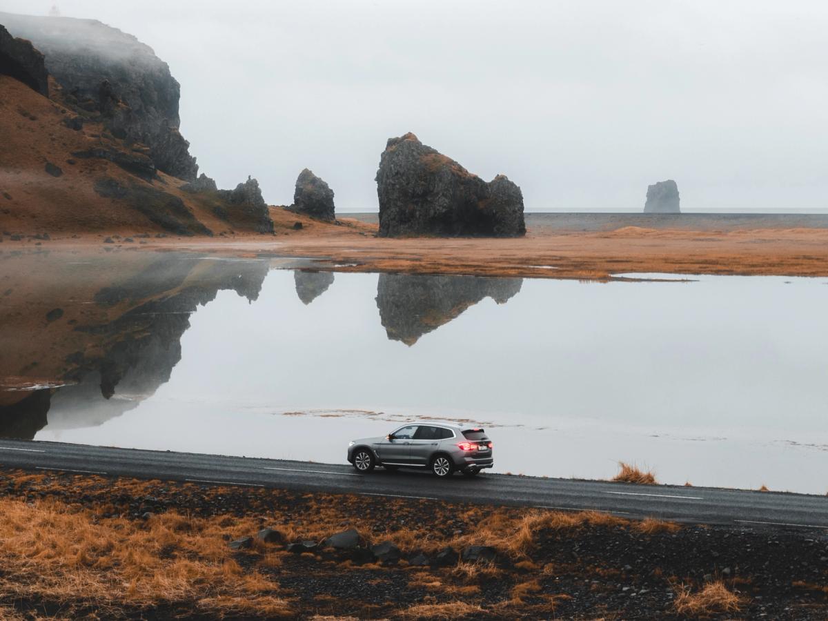 X3 Formations rocheuses côtières BMW X3 roulant sur une route côtière, avec des stacks marins se reflétant dans une eau calme