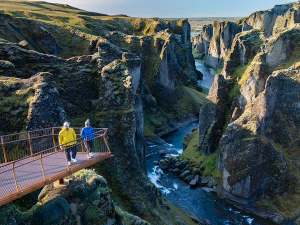Two hikers on an observation platform overlooking a deep, rocky canyon with a river.