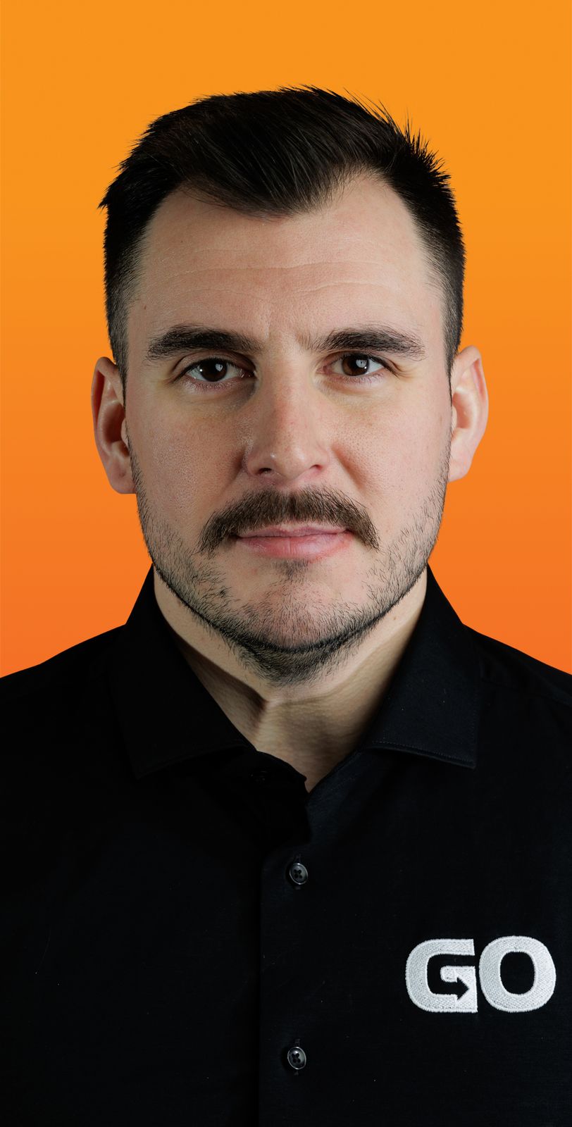 un homme avec une moustache porte une chemise noire qui dit GO