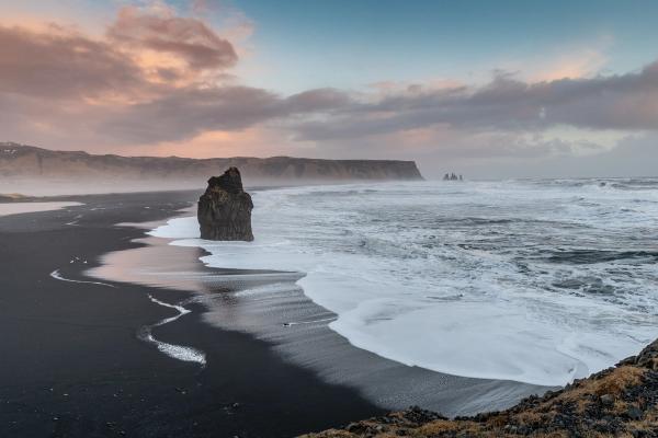 black sand beach with a rock in the middle