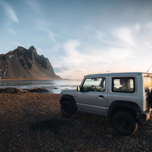 a silver jeep is parked on the beach next to a lake .