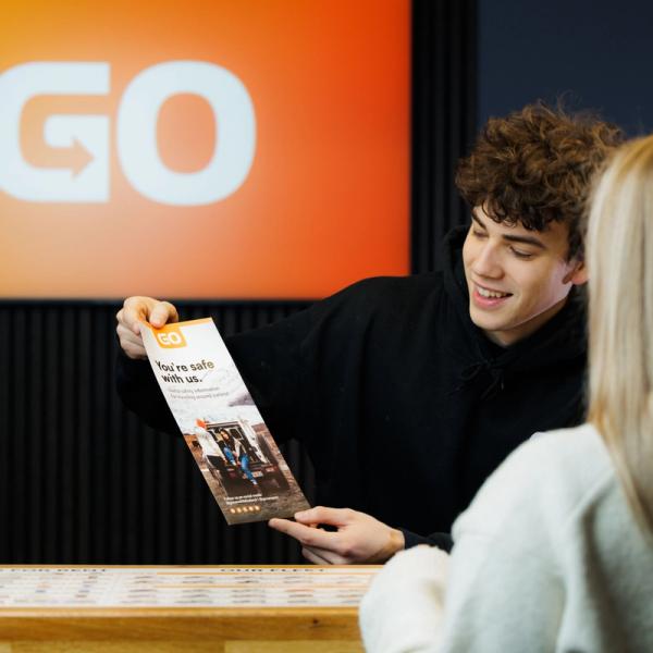 Un homme remet une brochure à une femme au comptoir.