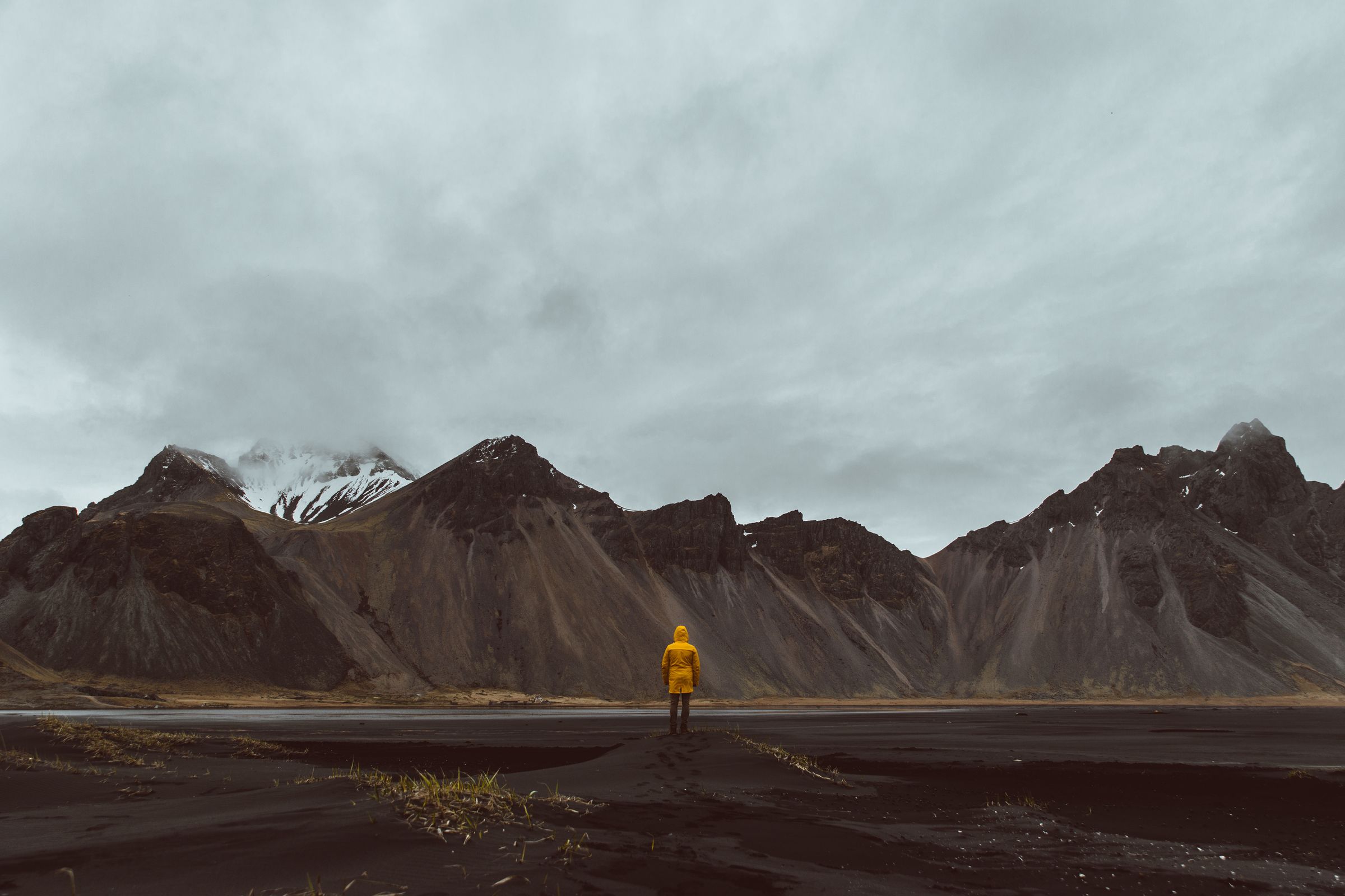 a man in a yellow raincoat is standing in front of a mountain range .