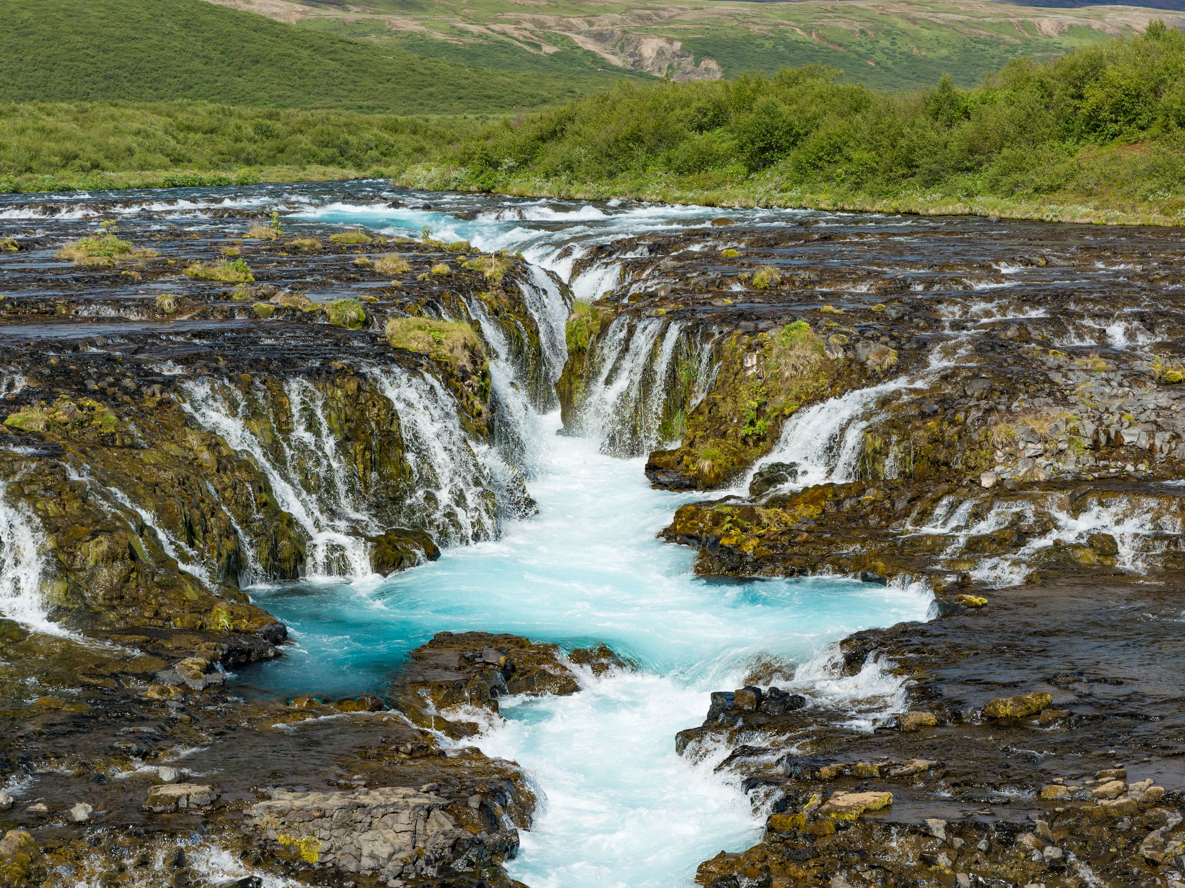 una cascada está rodeada de rocas y árboles en medio de un río .
