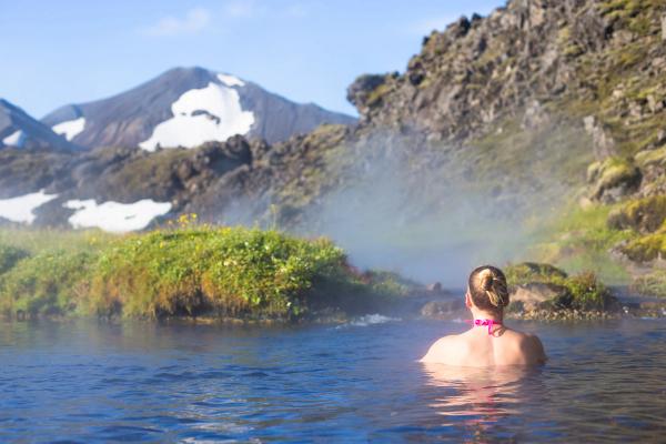 a woman is swimming in a hot spring in the mountains at landmannalaugar hot spring in iceland.