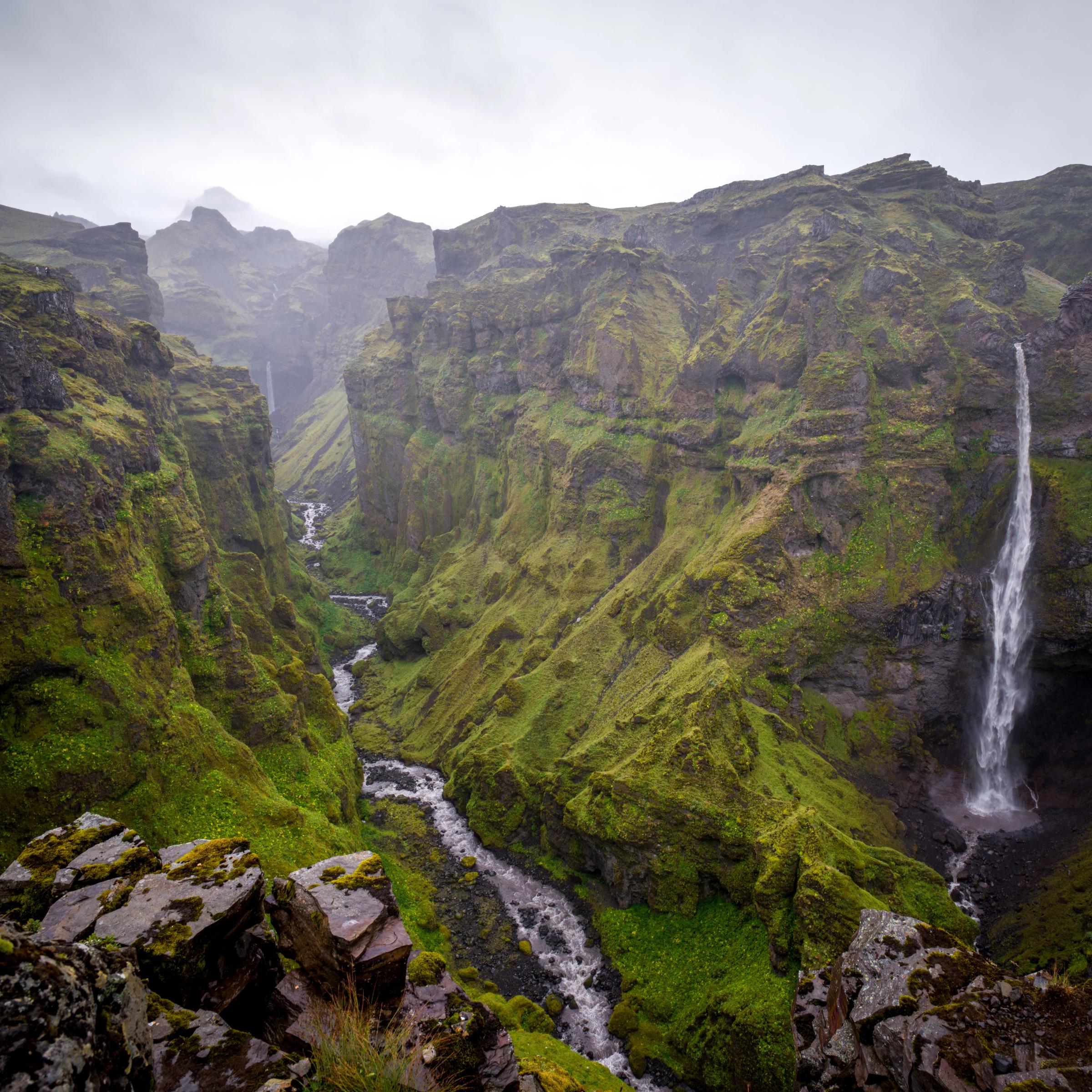 A deep, green canyon with a winding river and a tall waterfall on the right.