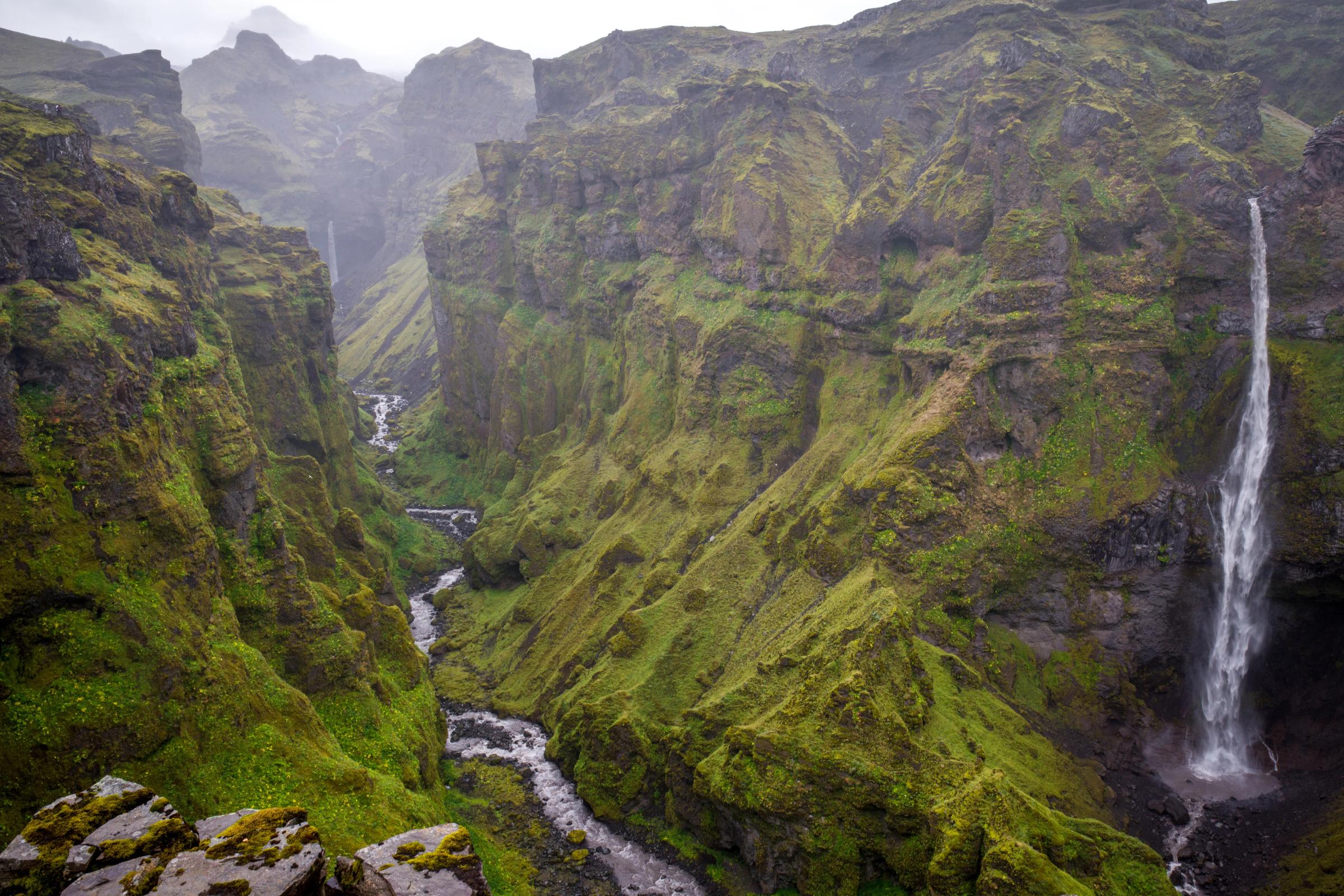 Un precioso cañón verde con un río en medio y una cascada enorme a su derecha