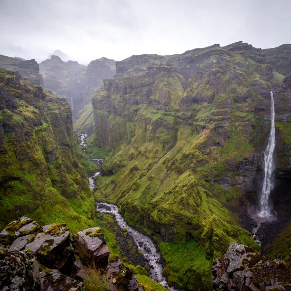 A deep, green canyon with a winding river and a tall waterfall on the right.