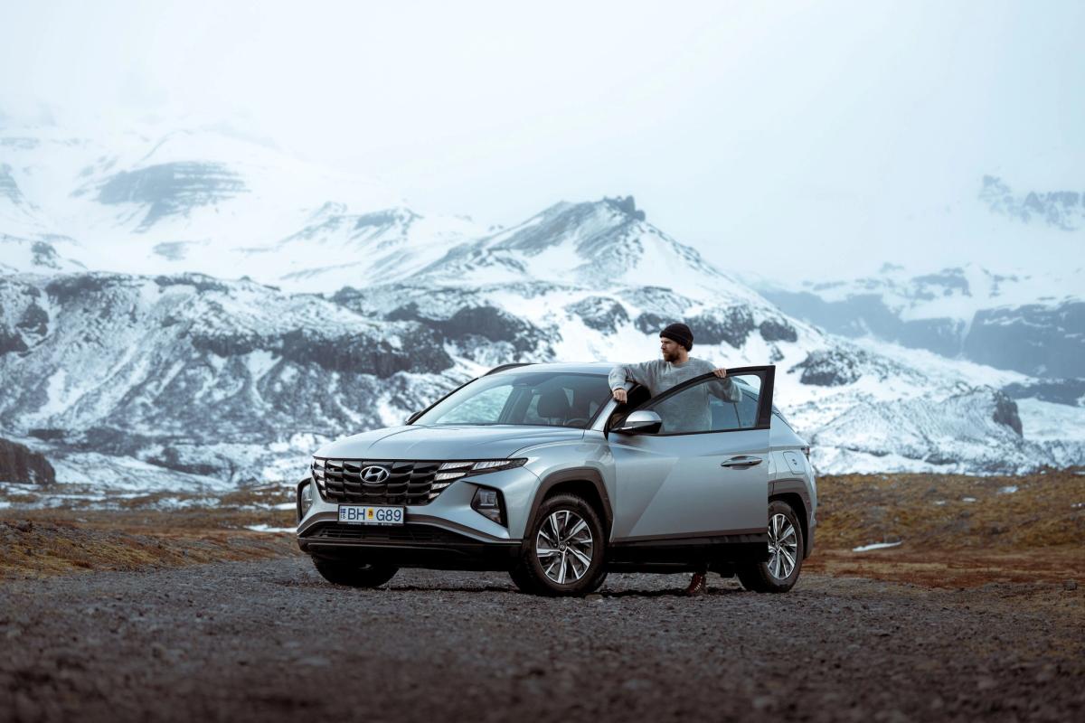 A person standing beside a Hyundai Tucson rental car in Iceland.