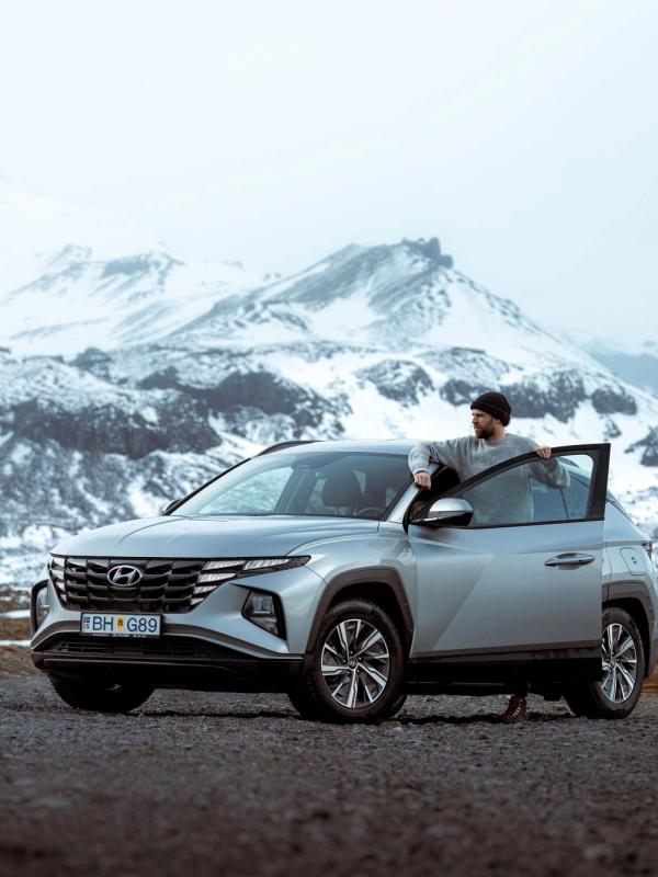 Gear up for your Icelandic adventure with our spacious and reliable Hyundai Tucson rental. A person standing beside a Hyundai Tucson rental car in Iceland.
