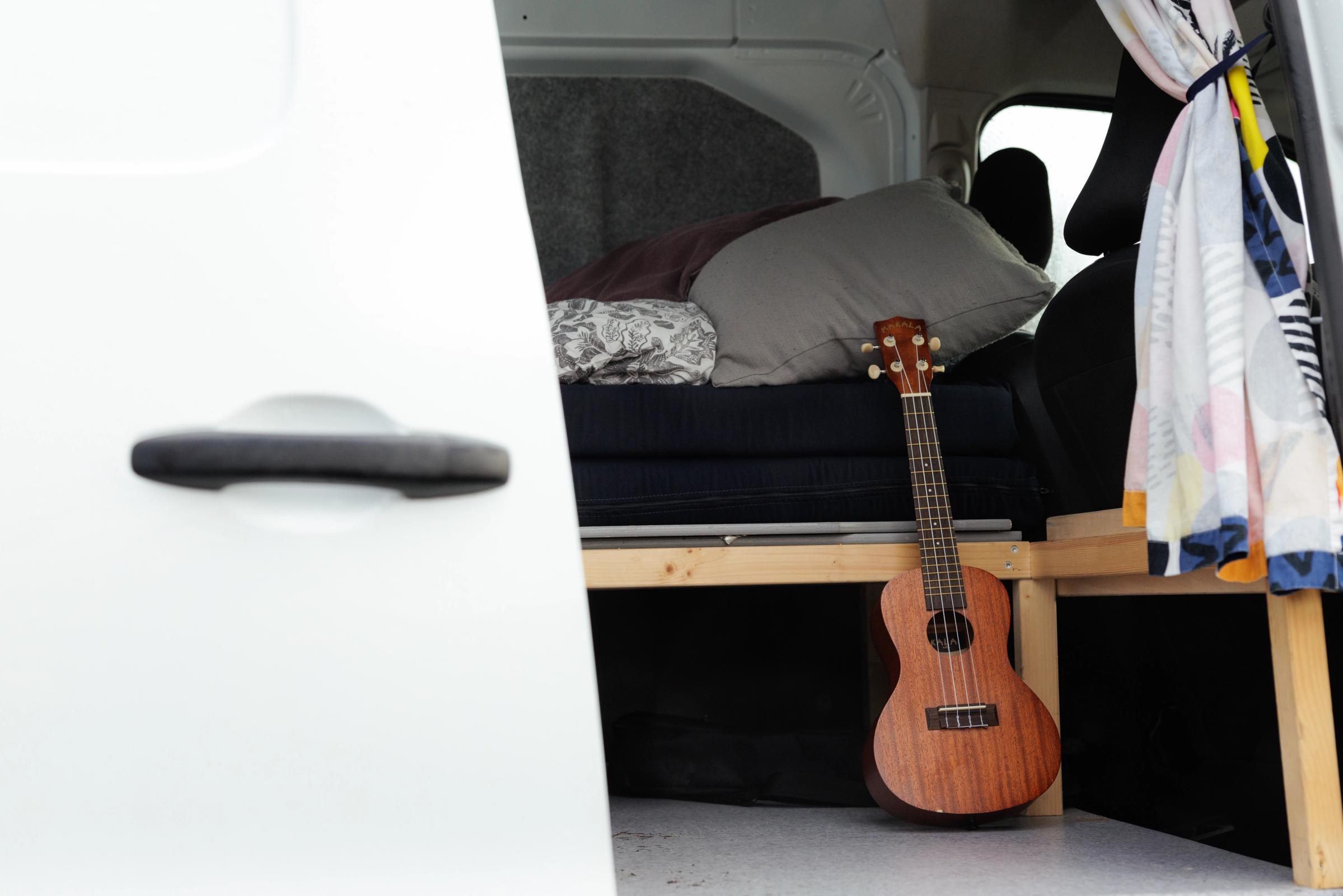 Eine Ukulele lehnt am hölzernen Bettrahmen, gesehen durch die offene Schiebetür