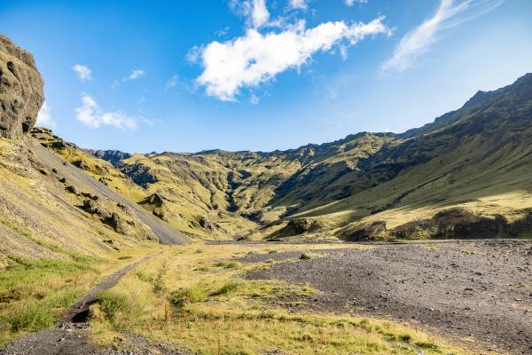 un chemin de terre traversant une vallée entourée de montagnes lors d'une journée ensoleillée.