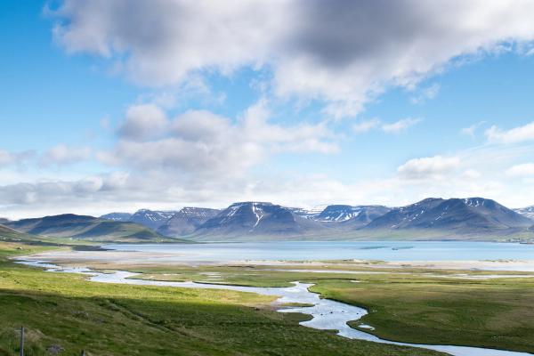 a river flowing through a grassy valley with mountains in the background .