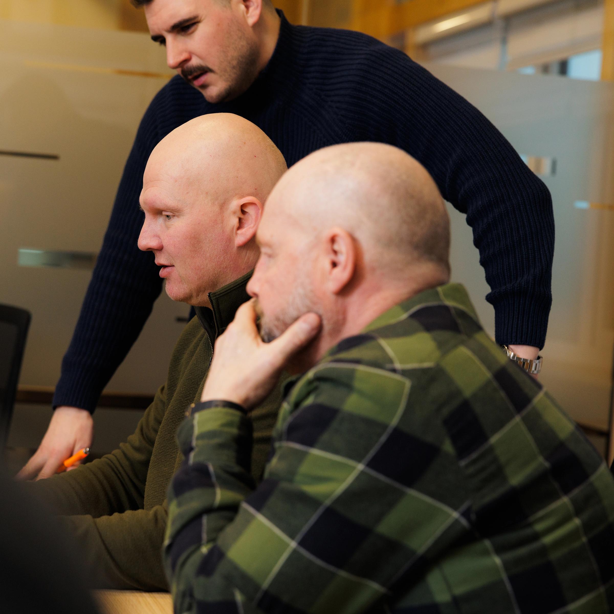 a group of men are looking at a computer screen together .