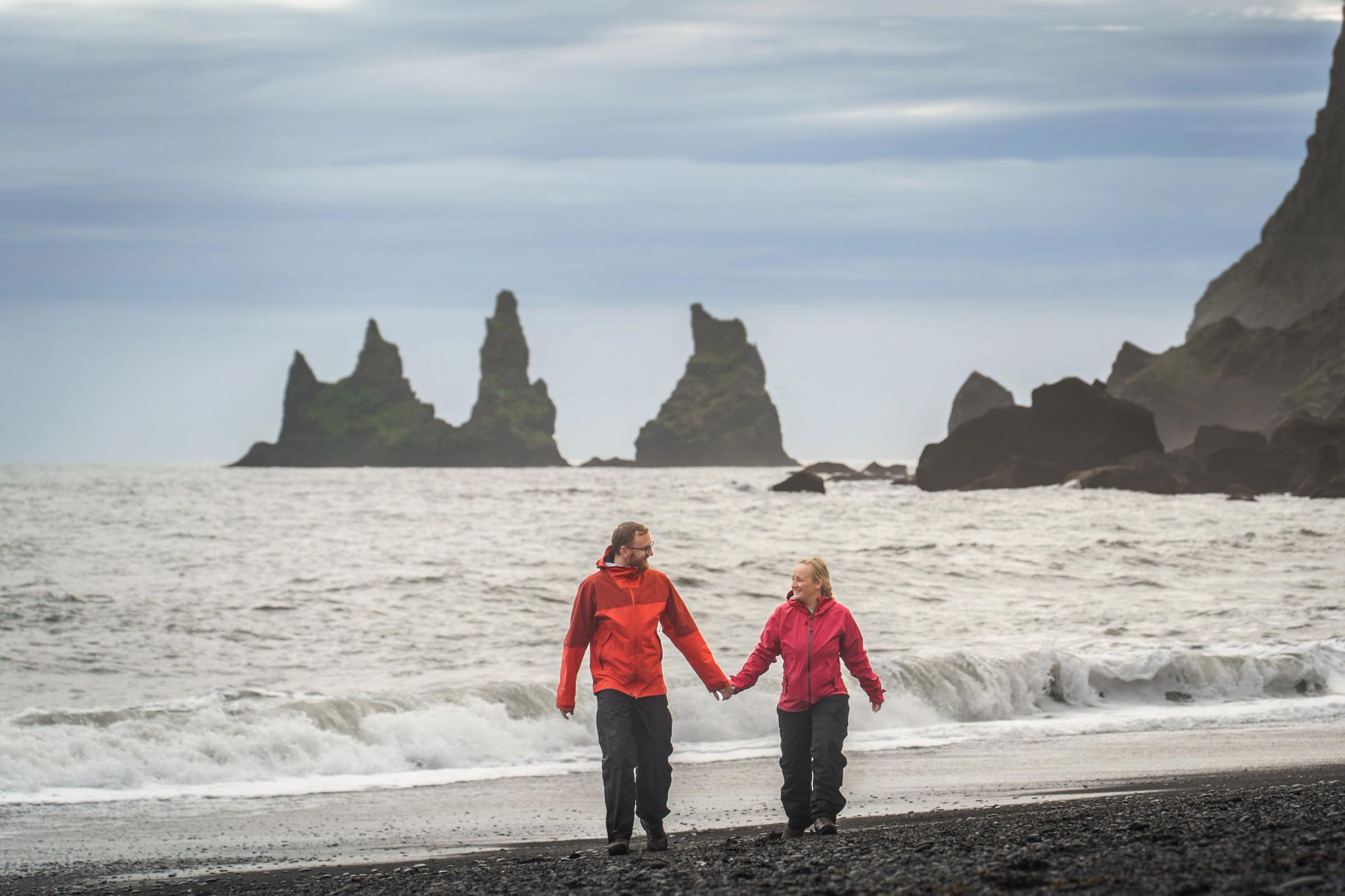 a couple with red jackets holding hands on a black sand beach