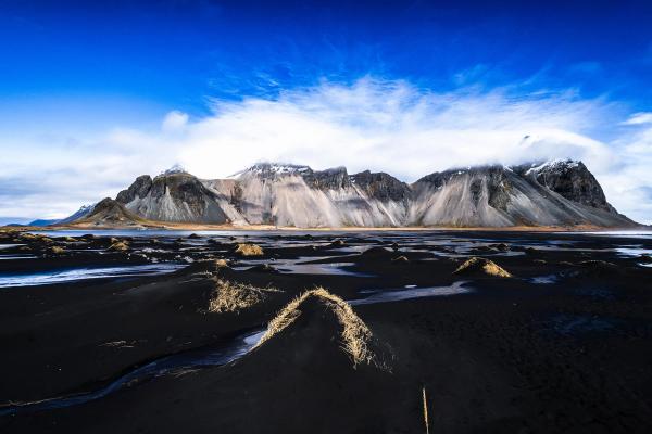 un lago con una montaña al fondo y una colina cubierta de hierba en primer plano.