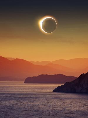 Solar eclipse above lake and mountains