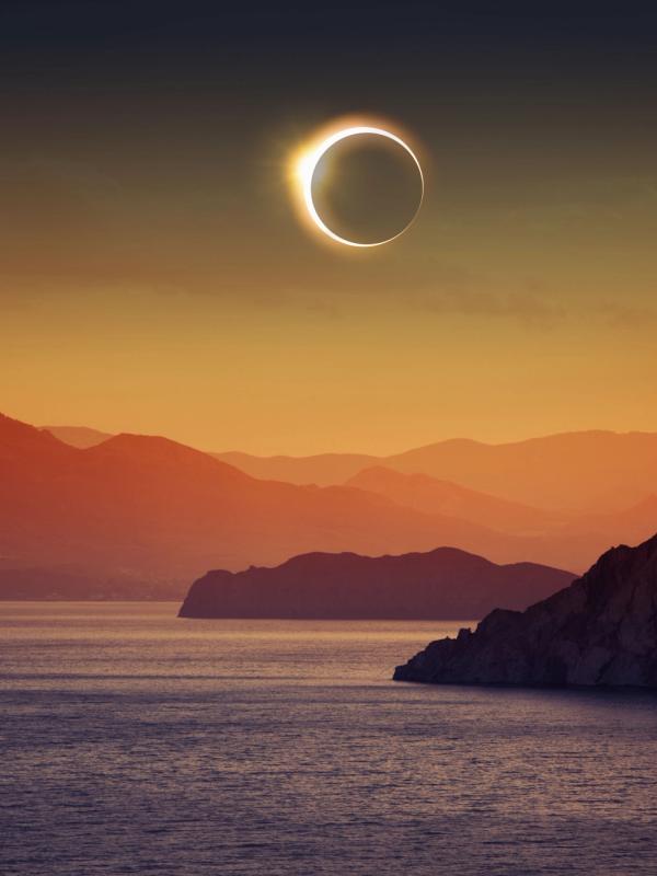 Solar eclipse above lake and mountains