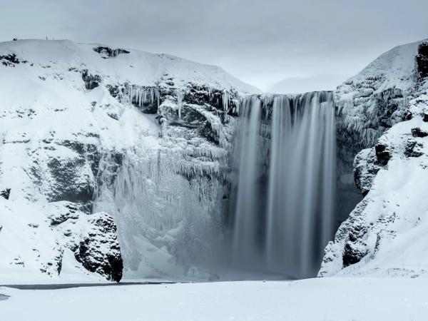 a waterfall is surrounded by snow covered mountains and rocks .