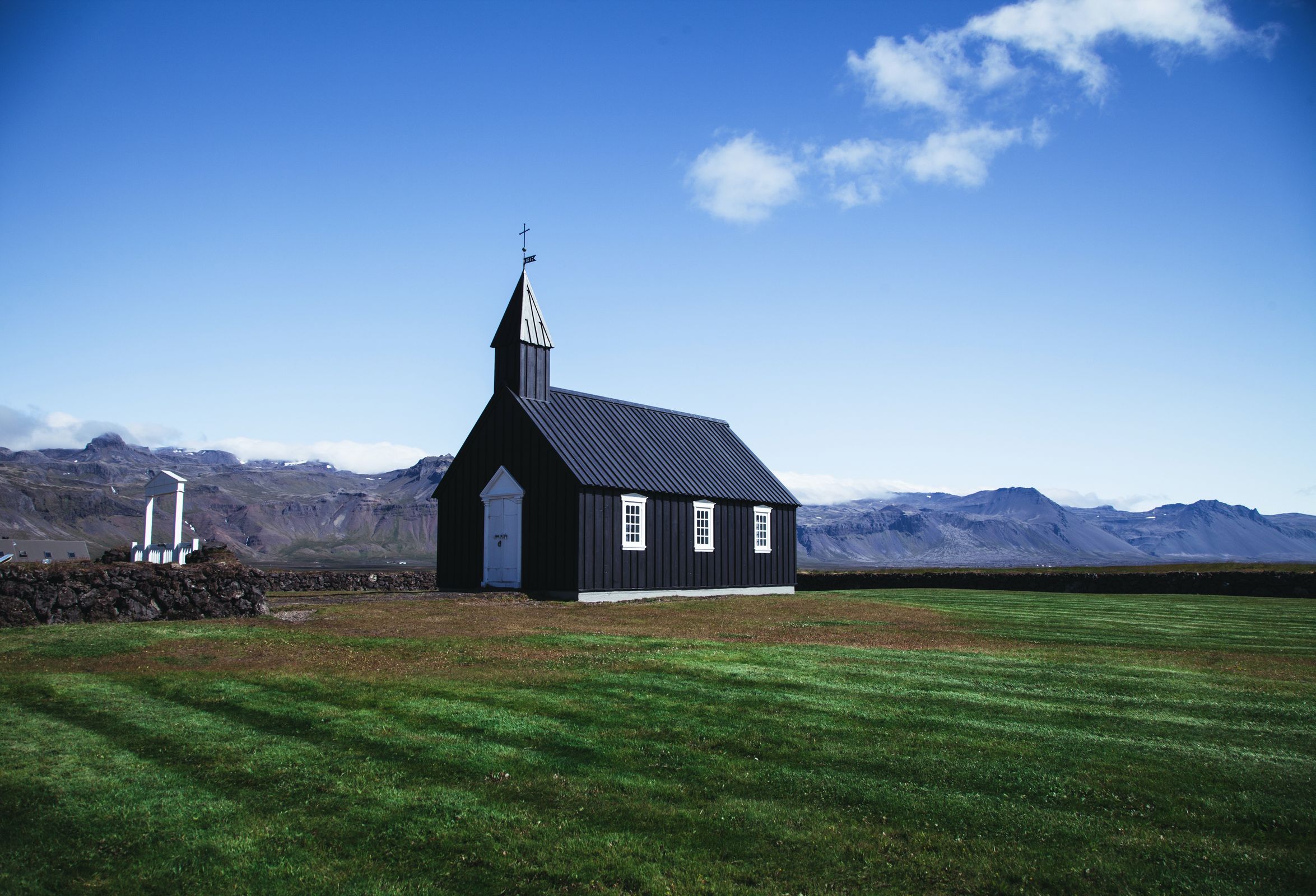 a small black church is sitting in the middle of a grassy field with mountains in the background .