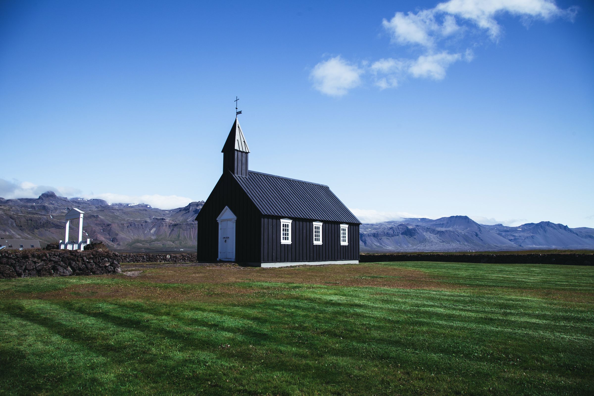 a small black church is sitting in the middle of a grassy field with mountains in the background .