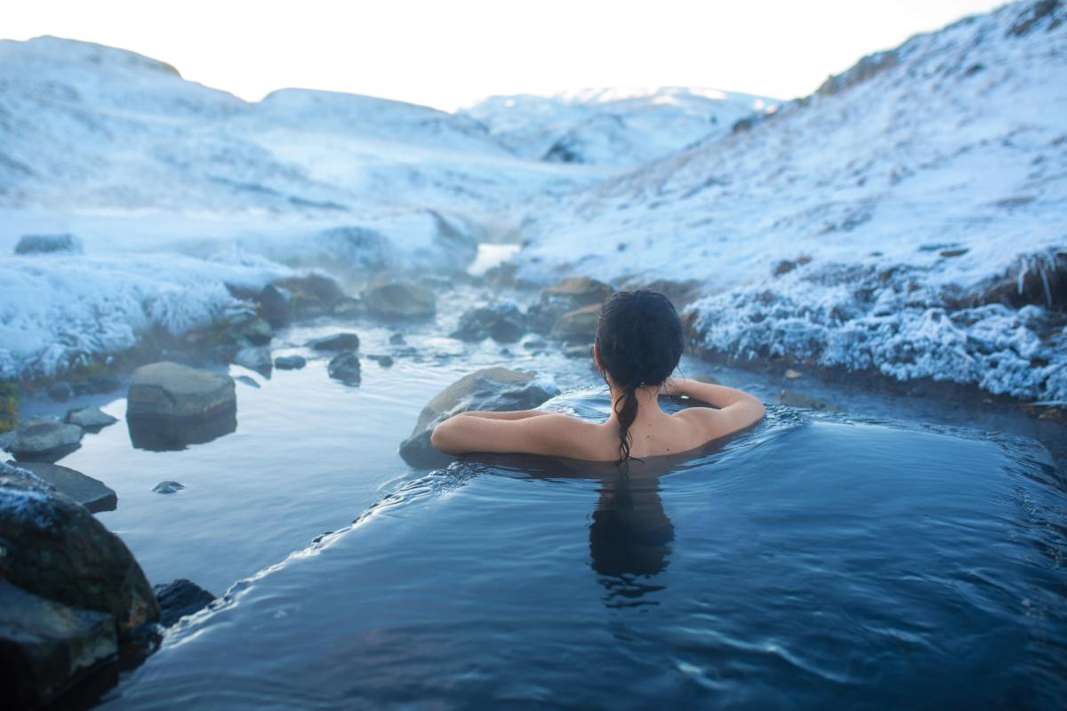 a woman is taking a bath in a hot spring in the mountains in iceland.