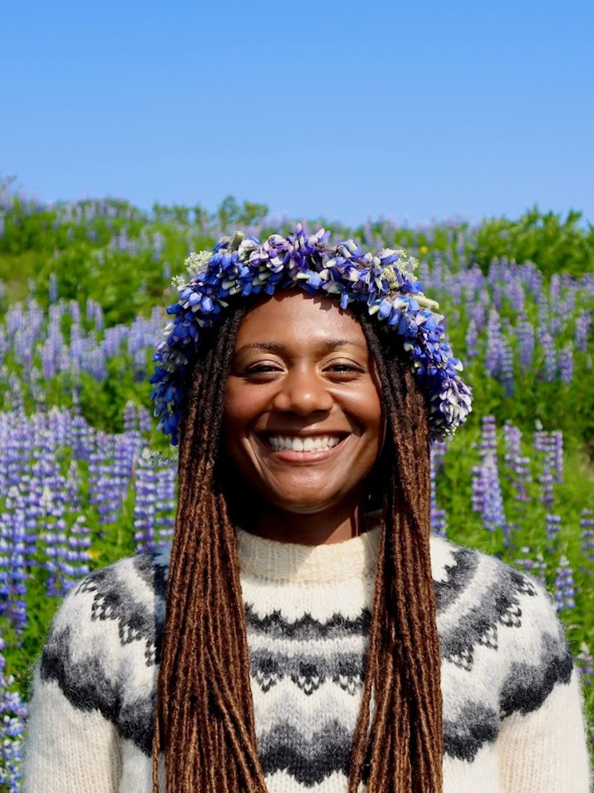 a woman wearing a flower crown is smiling in a field of purple flowers .