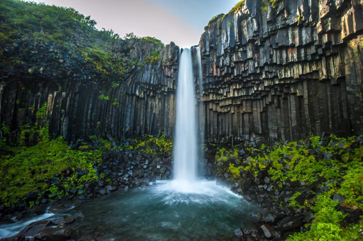 Waterfall cascading over dark hexagonal basalt columns with green moss.