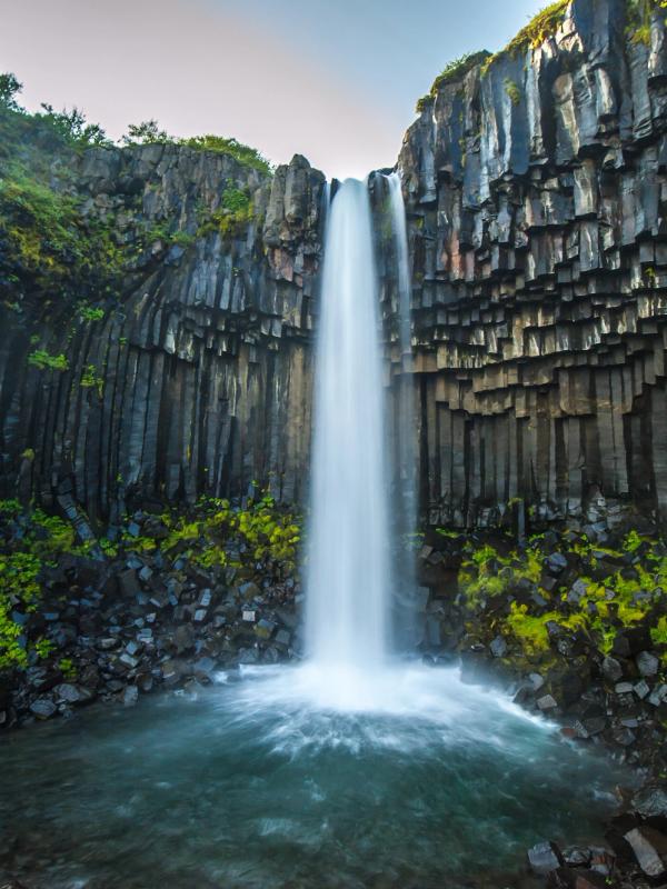 Waterfall cascading over dark hexagonal basalt columns with green moss.
