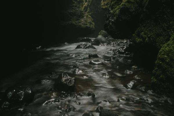 Stream flowing over rocks in a dark, mossy canyon with distant light.