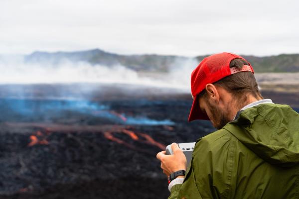 a man in a red hat is taking a picture of Litli-Hrutur volcano .