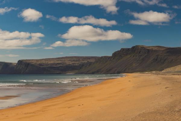 a golden sand beach with cliffs on the background