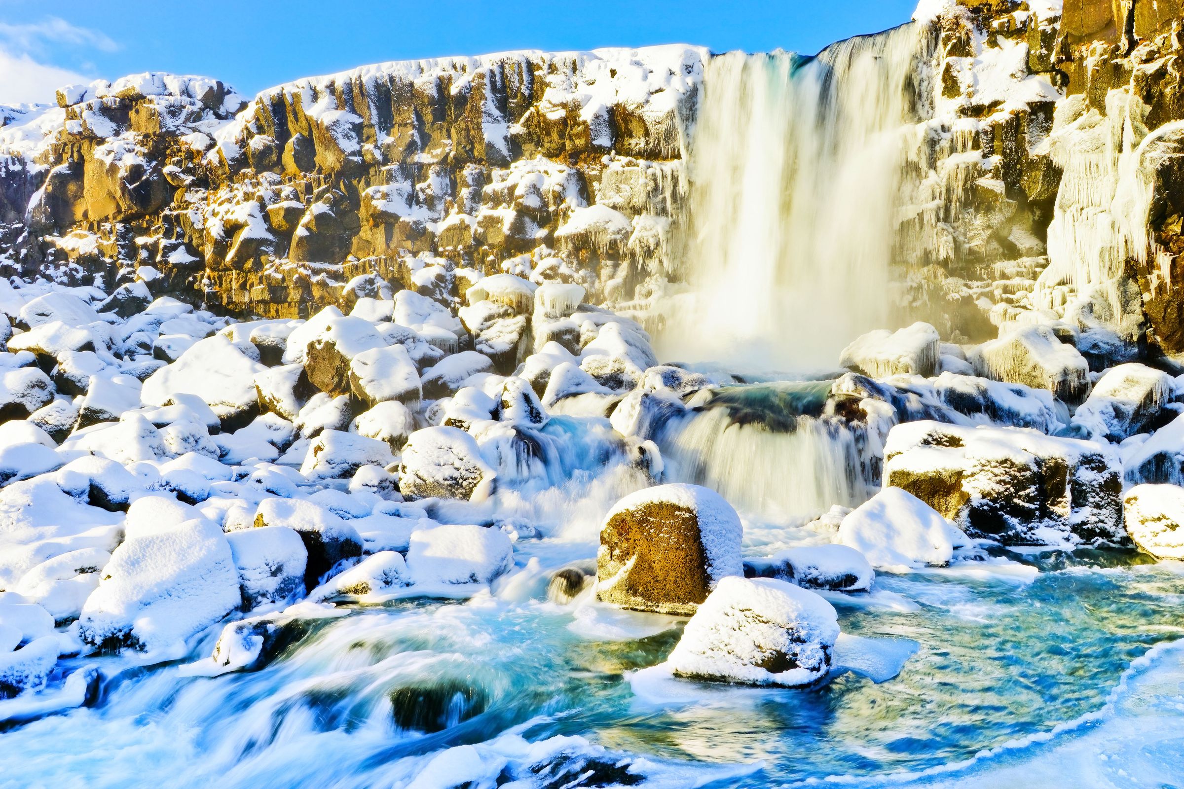 a waterfall is surrounded by snow covered rocks and a river at Þingvellir in iceland.