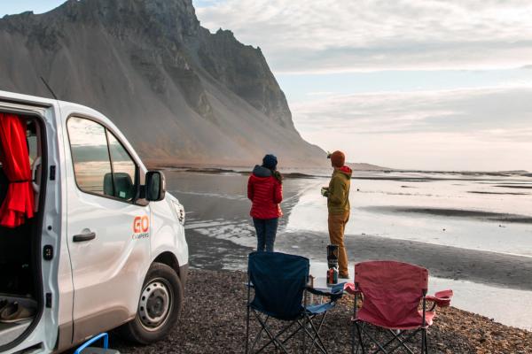 a white van with and two people outside next to a beach in Iceland