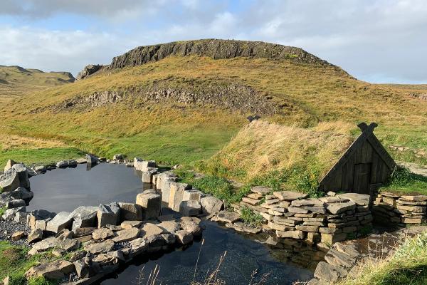 there is a small house in the middle of a field next to a pond .