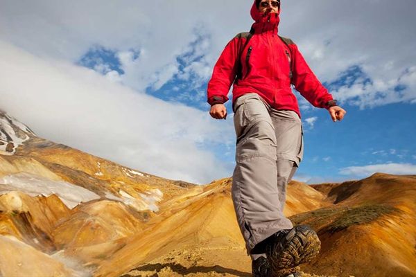a man in a red jacket is walking across a mountain in iceland.