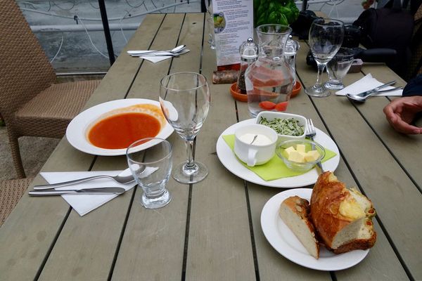Tomato soup, bread, butter, cream, and greens arranged on a wooden table.