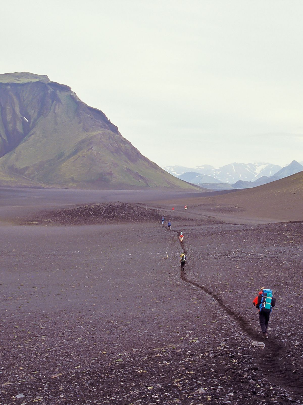 a person with a backpack is walking through a desert with mountains in the background .